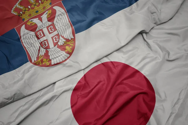 Vinka färgglada flagga av Japan och nationella flaggan Serbien. — Stockfoto