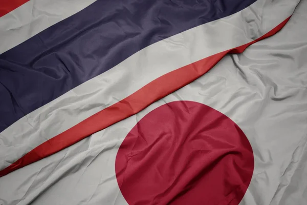 waving colorful flag of japan and national flag of thailand.