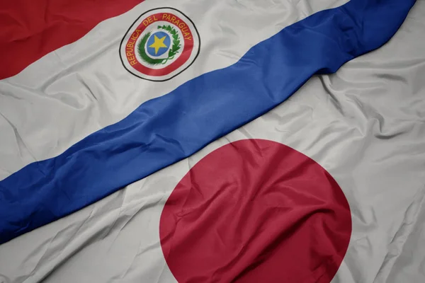 waving colorful flag of japan and national flag of paraguay.