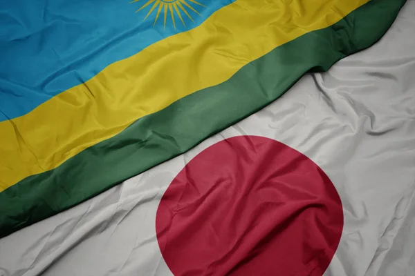 waving colorful flag of japan and national flag of rwanda.