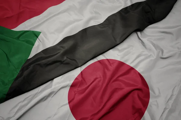 waving colorful flag of japan and national flag of sudan.