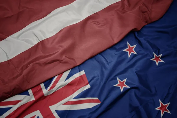 Acenando bandeira colorida de Nova Zelândia e bandeira nacional de latvia . — Fotografia de Stock
