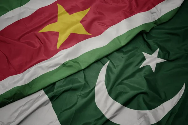 Ondeando colorida bandera de Pakistán y bandera nacional de Surinam . — Foto de Stock