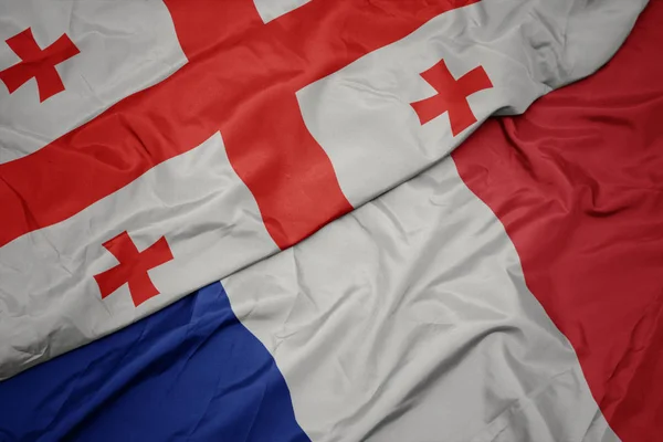 Zwaaiende kleurrijke vlag van Frankrijk en de nationale vlag van Georgië. — Stockfoto