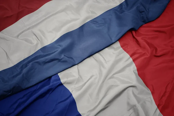 Zwaaiende kleurrijke vlag van Frankrijk en de nationale vlag van Nederland. — Stockfoto