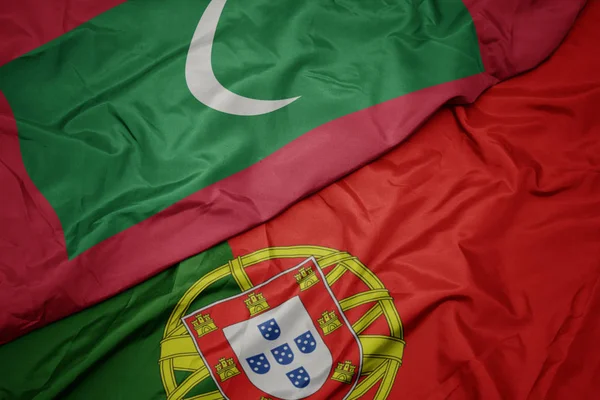 waving colorful flag of portugal and national flag of maldives.