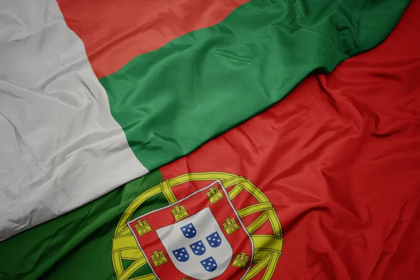 Acenando bandeira colorida de portugal e bandeira nacional de madagáscar . — Fotografia de Stock