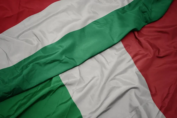Ondeando colorida bandera de italia y bandera nacional de hungary . —  Fotos de Stock