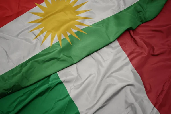 Falujące kolorowe flagi Włoch i flagi narodowej Kurdystanu. — Zdjęcie stockowe