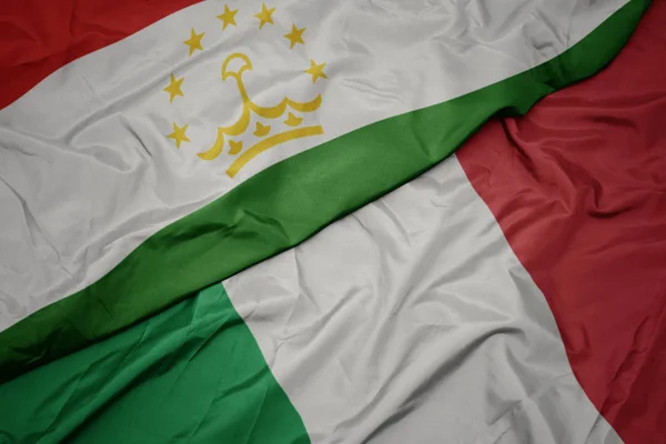Acenando bandeira colorida de itália e bandeira nacional do tajiquistão . — Fotografia de Stock
