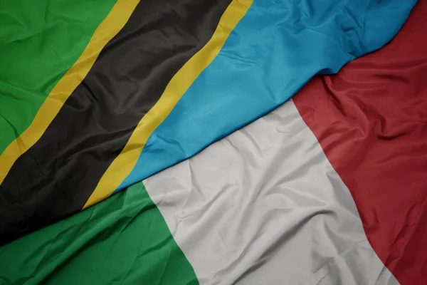 Ondeando colorida bandera de italia y bandera nacional de tanzania . —  Fotos de Stock