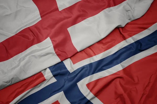 Zwaaiende kleurrijke vlag van Noorwegen en de nationale vlag van Engeland. — Stockfoto