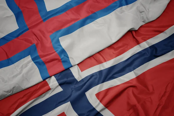 Zwaaiende kleurrijke vlag van Noorwegen en de nationale vlag van Faeröer. — Stockfoto