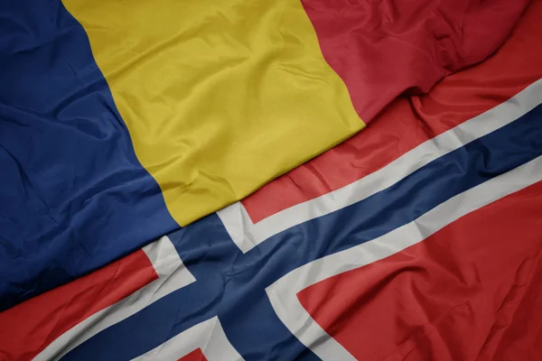 Zwaaiende kleurrijke vlag van Noorwegen en de nationale vlag van Roemenië. — Stockfoto