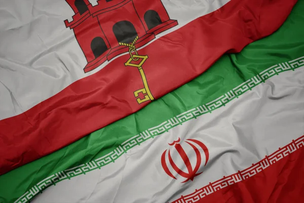 Zwaaiende kleurrijke vlag van Iran en de nationale vlag van Gibraltar. — Stockfoto