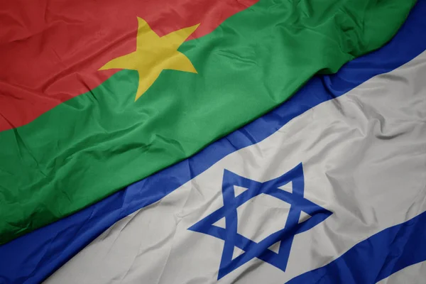 Zwaaiende kleurrijke vlag van Israël en de nationale vlag van Burkina Faso. — Stockfoto