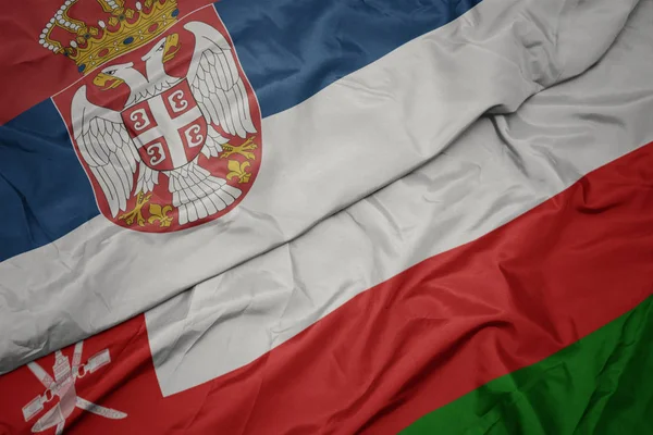 Mávající barevná vlajka Ománu a národní vlajky Srbska. — Stock fotografie
