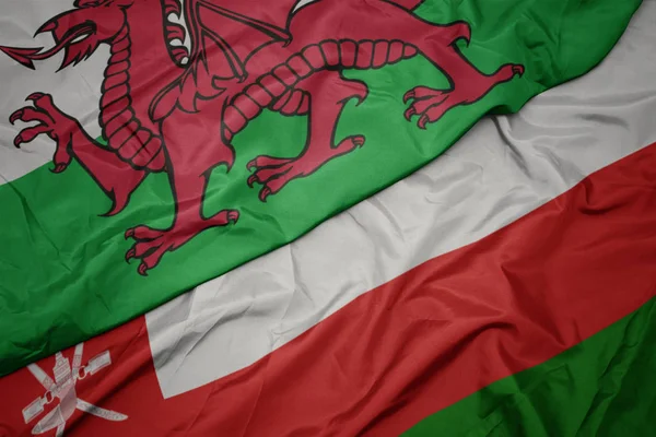 Zwaaiende kleurrijke vlag van Oman en de nationale vlag van Wales. — Stockfoto