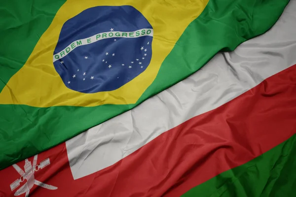 Agitant drapeau coloré d'oman et drapeau national du Brésil . — Photo