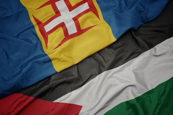 waving colorful flag of palestine and national flag of madeira.