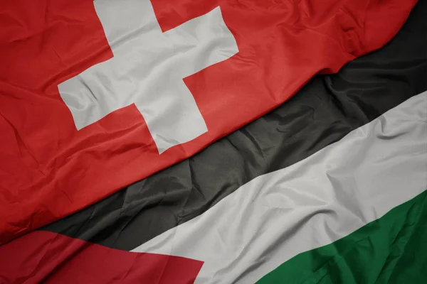 waving colorful flag of palestine and national flag of switzerland.