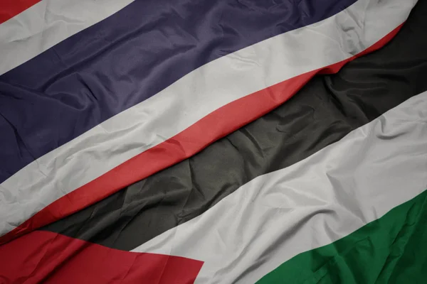 waving colorful flag of palestine and national flag of thailand.