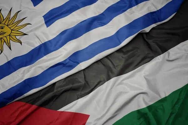 waving colorful flag of palestine and national flag of uruguay.