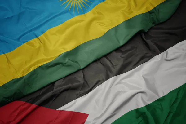 waving colorful flag of palestine and national flag of rwanda.