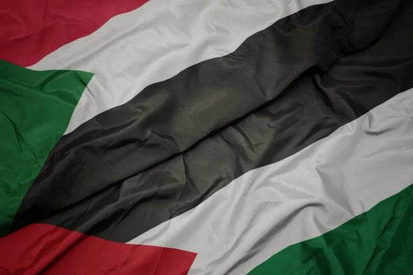 waving colorful flag of palestine and national flag of sudan.