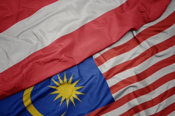 Zwaaiende kleurrijke vlag van Maleisië en de nationale vlag van Oostenrijk. — Stockfoto