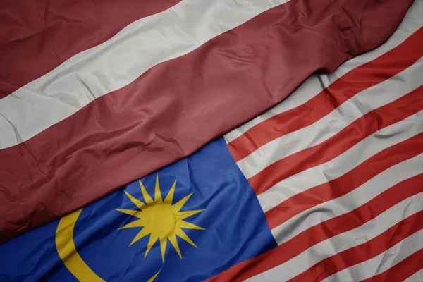 Sventolando bandiera colorata di malesia e bandiera nazionale di latvia . — Foto Stock
