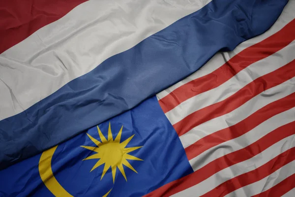 Viftande färgglada flagga av Malaysia och nationella flaggan i Nederländerna. — Stockfoto