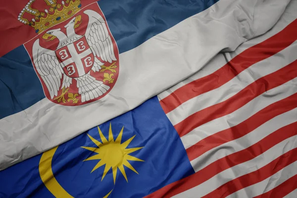 Zwaaiende kleurrijke vlag van Maleisië en de nationale vlag van Servië. — Stockfoto