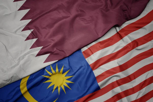 Mávající barevnou vlajku Malajsie a národní vlajky Kataru. — Stock fotografie