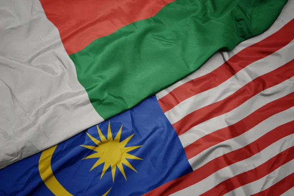 Sventolando bandiera colorata di malesia e bandiera nazionale di madagvania . — Foto Stock