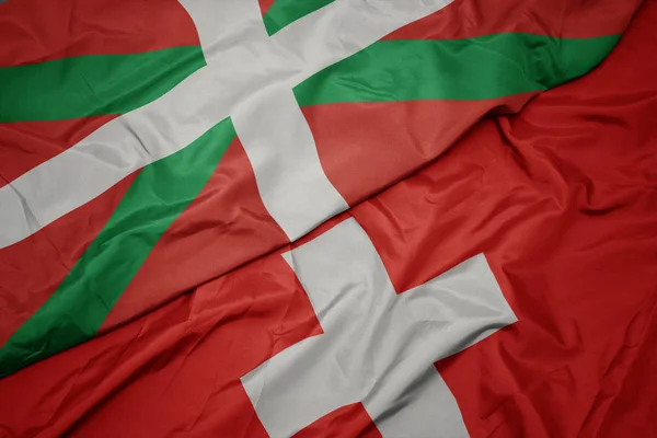 Falujące kolorowe flagi Szwajcarii i flagi narodowej kraju Basków. — Zdjęcie stockowe