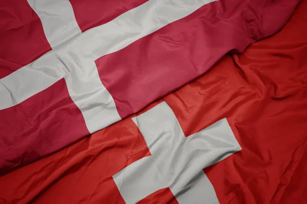 Agitant drapeau coloré de la Suisse et drapeau national du Danemark . — Photo