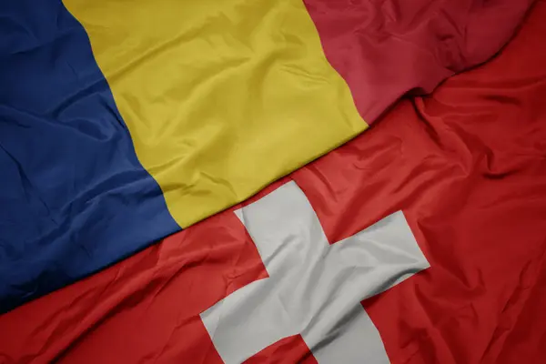 Acenando bandeira colorida da Suíça e bandeira nacional da Romênia . — Fotografia de Stock