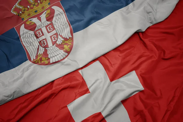Acenando bandeira colorida da Suíça e bandeira nacional da Sérvia . — Fotografia de Stock