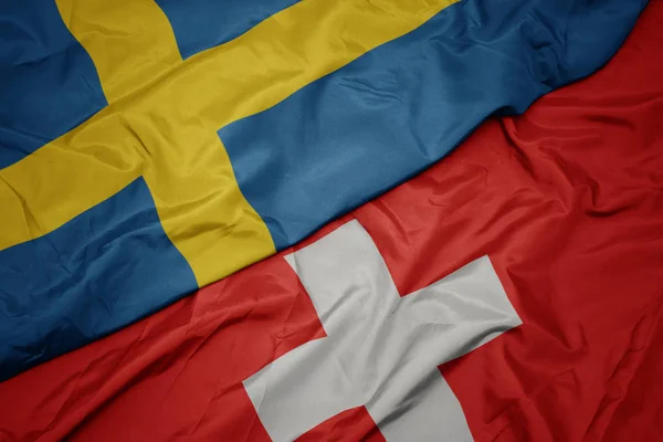 Waving colorful flag of switzerland and national flag of sweden. — Stok Foto