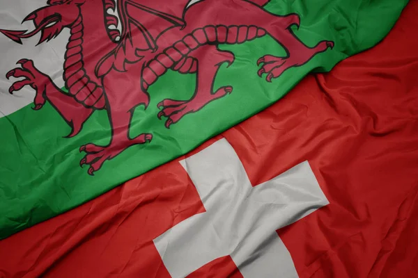 Mávající barevná vlajka Švýcarska a národní vlajka Walesu. — Stock fotografie