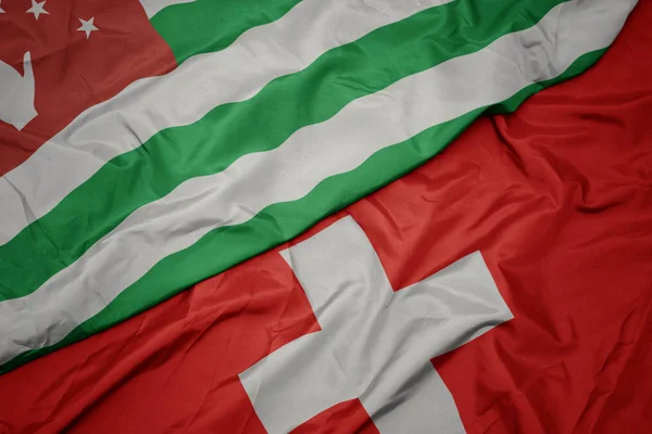 Ondeando colorida bandera de Suiza y bandera nacional de abjasia . — Foto de Stock