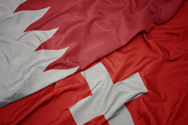 waving colorful flag of switzerland and national flag of bahrain.