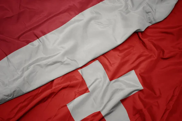 Schwenkt die bunte Flagge der Schweiz und die Nationalflagge Indonesiens. — Stockfoto