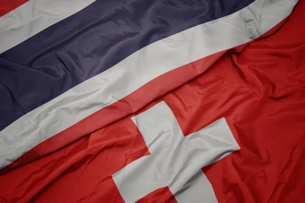 Mávající barevná vlajka Švýcarska a národní vlajka Thajska. — Stock fotografie