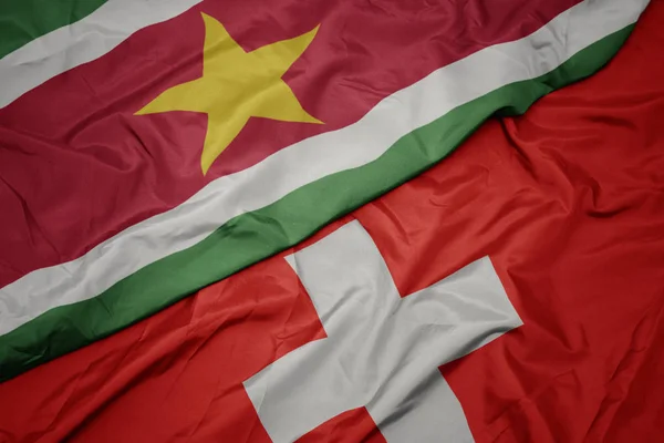 Ondeando colorida bandera de Suiza y bandera nacional de Surinam . — Foto de Stock