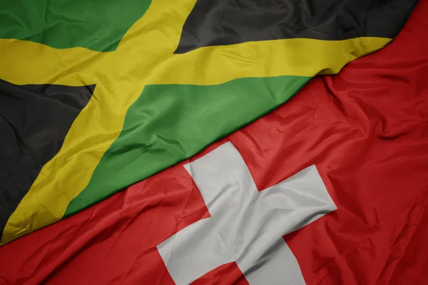 Ondeando colorida bandera de Suiza y bandera nacional de jamaica . —  Fotos de Stock