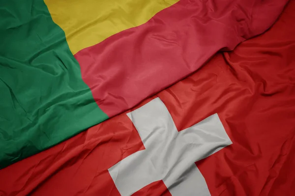 Mávající barevná vlajka Švýcarska a národní vlajka Benin. — Stock fotografie