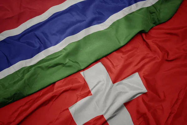 Sventolando bandiera colorata della Svizzera e bandiera nazionale della Gambia . — Foto Stock