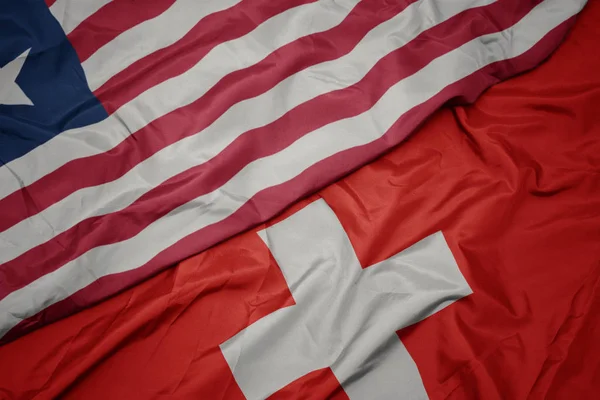 waving colorful flag of switzerland and national flag of liberia.